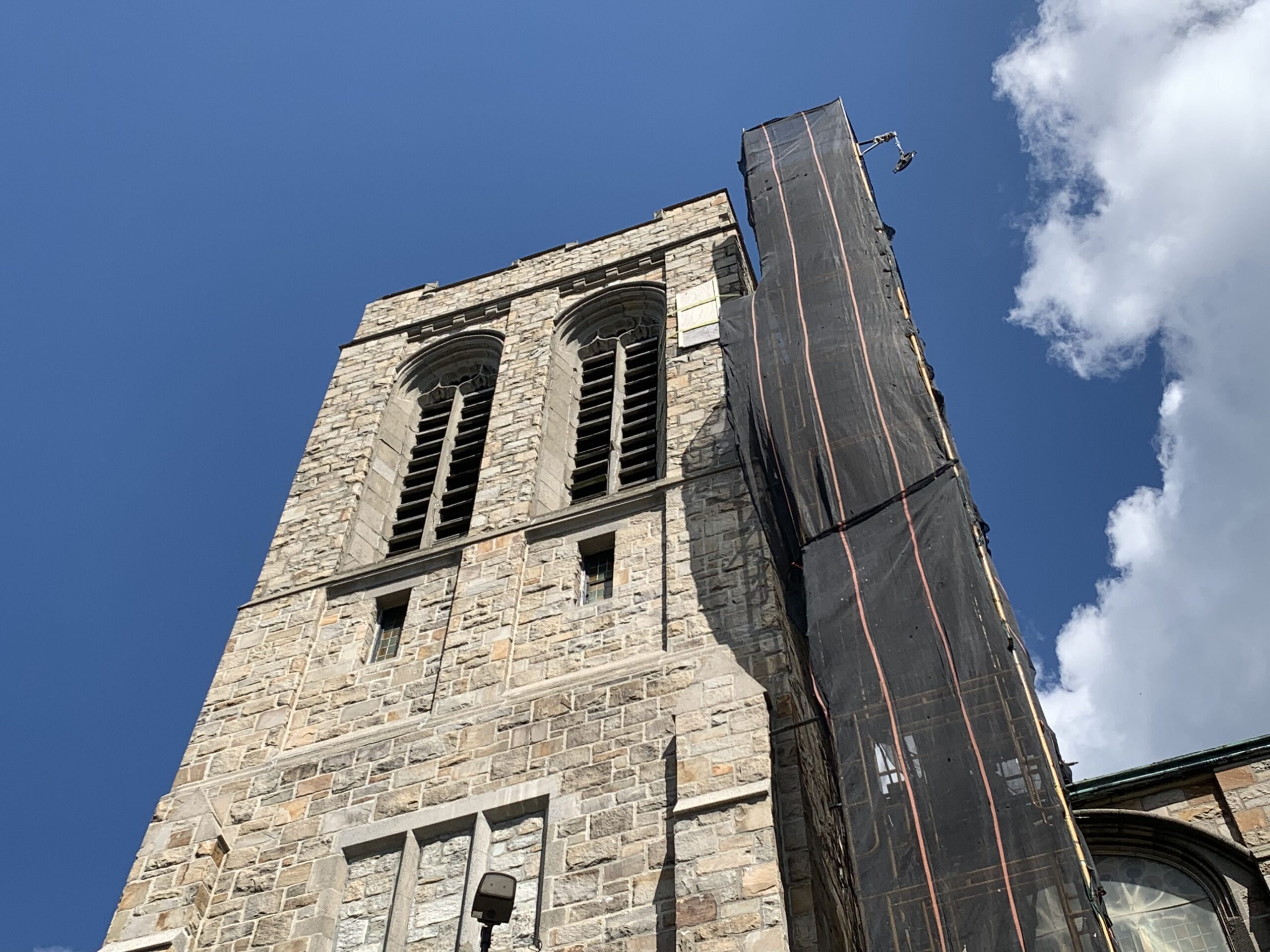 The stone church tower against a blue sky with protective netting and scaffolding along one side