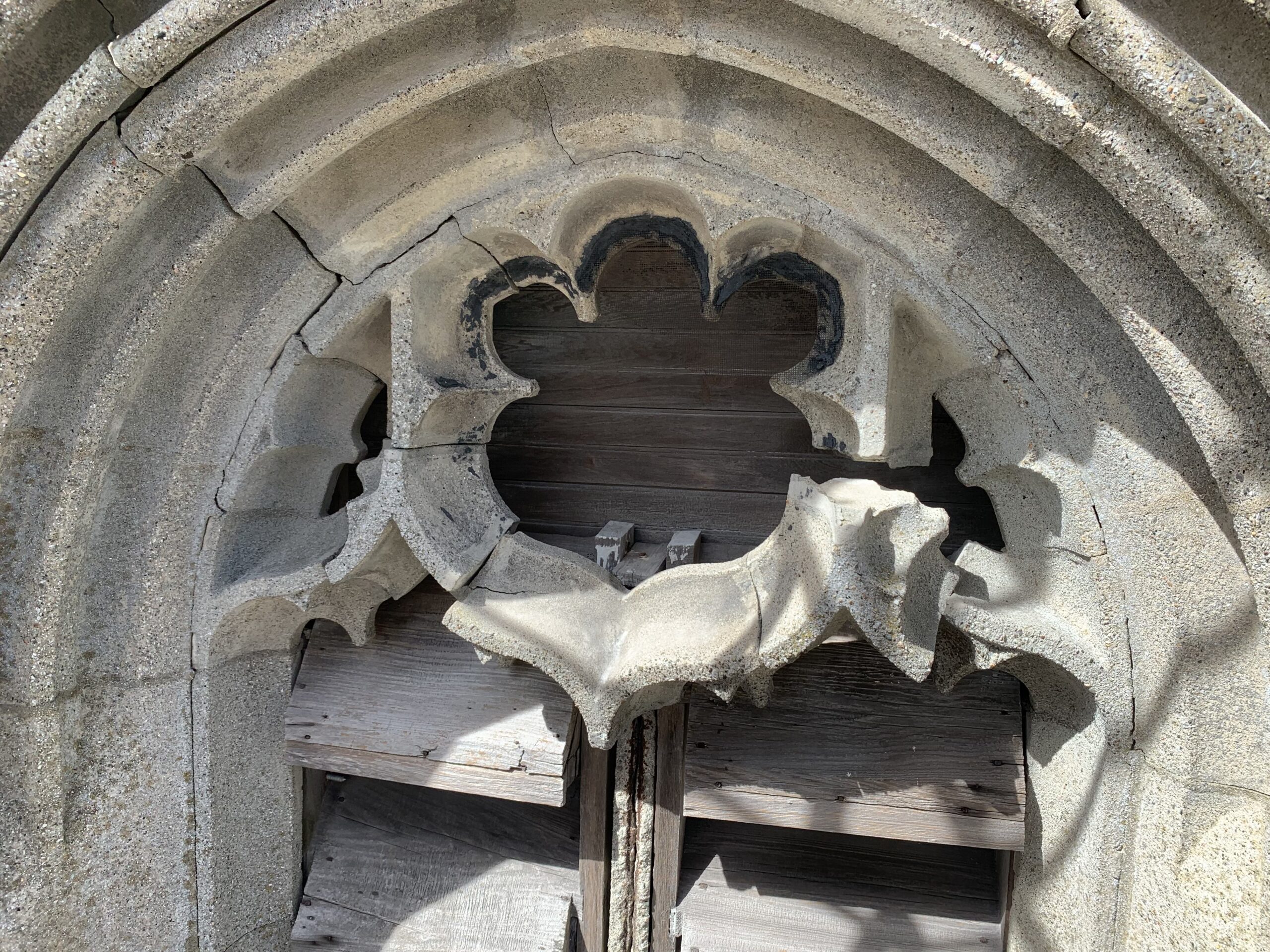 Close view of carved stone above a tower opening, with visible cracks and gaps around the decorative detail