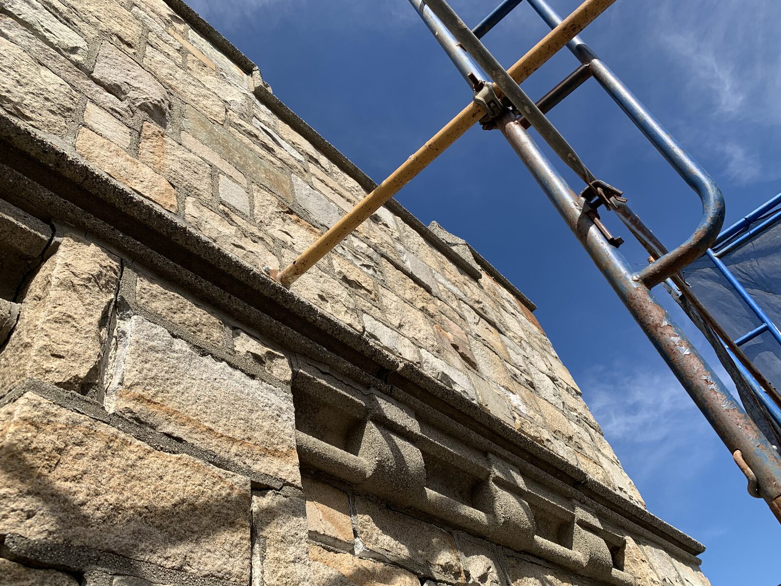 Historic stone cornice and upper wall photographed beside restoration scaffolding