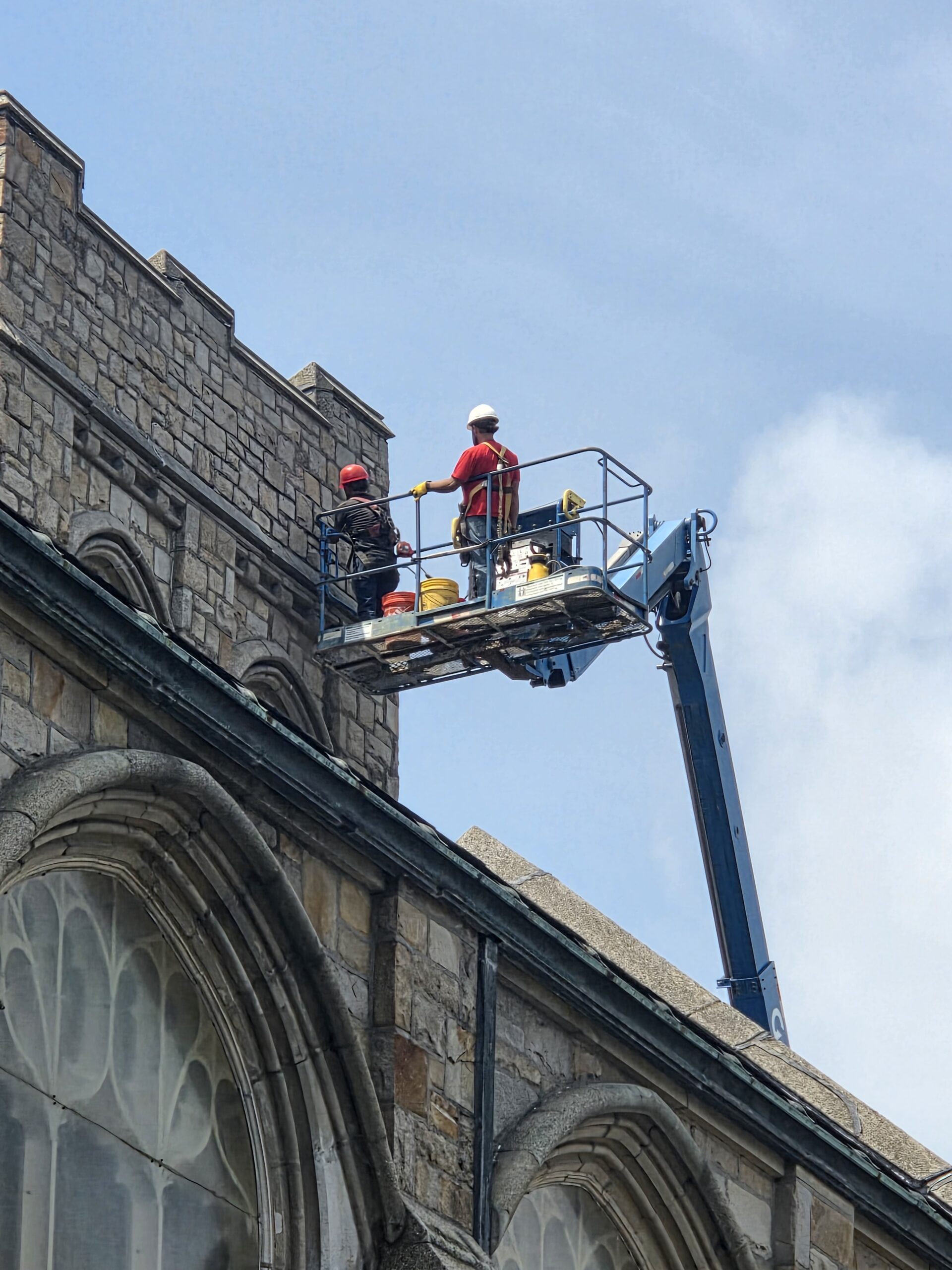Historic masonry workers restoring the Christ The Rock Church tower from a lift